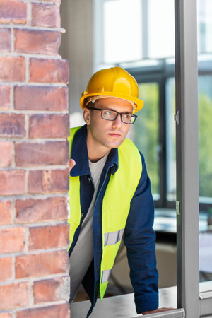 male builder in helmet looking out windowの写真素材