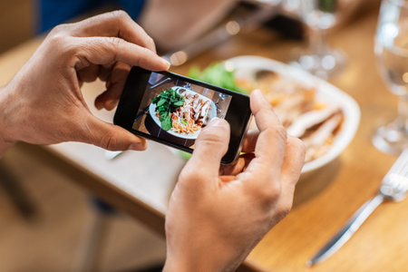 man with phone photographing food at restaurantの写真素材