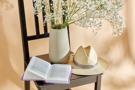 flowers in vase, book and straw hat on chairの写真素材