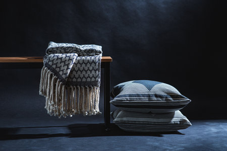 blanket on bench and pillows on floor in dark roomの写真素材