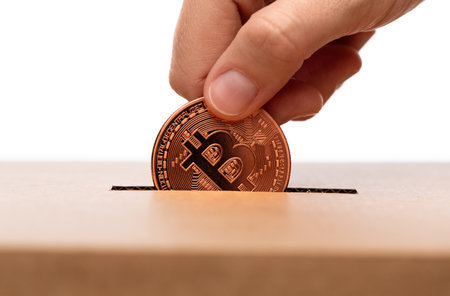 hand putting bitcoin into charity donation boxの写真素材