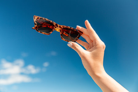 close up of hand holding sunglasses over blue skyの写真素材