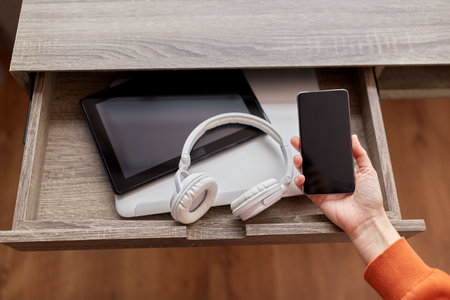hand with smartphone and gadgets in desk drawerの写真素材