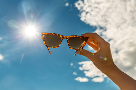 close up of hand holding sunglasses over blue skyの写真素材