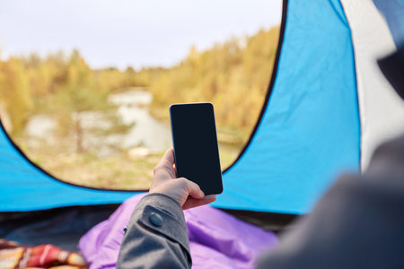 woman with phone in sleeping bag in camp tentの写真素材