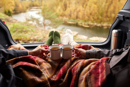 couple under blanket drinking tea in car trunk