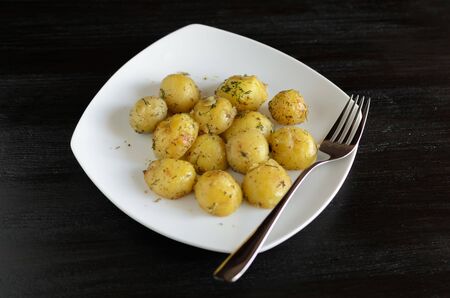 Roasted small potato tubers with spices on white plate.