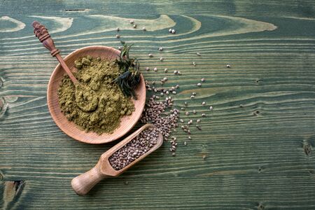 Composition with wooden bowl of hemp protein powder, cannabis seeds on wooden table. Space for textの写真素材