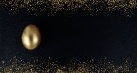 Minimal gold eggs easter concept. Golden egg with golden shine decorated confetti for banner, greeting card, social media advertise.Gold on black stone.Flat lay trendy easter greeting card copy spaceの写真素材
