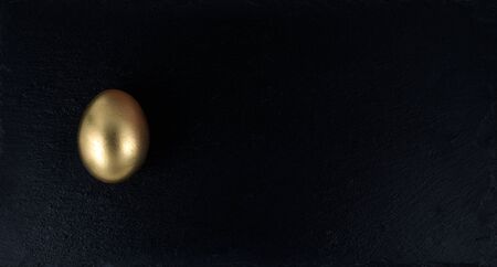 Minimal gold eggs easter concept. Stylish easter golden egg with black stone tray, white wooden background. Flat lay trendy easter. Happy easter card.Copy space for text on black boardの写真素材