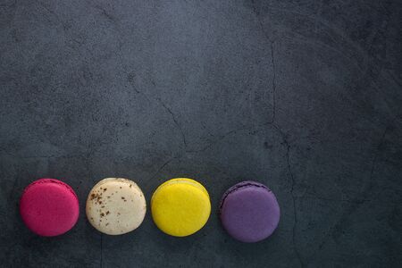 Colourful minimalistic greeting card concept. Different colours french macaroons on black grunge stone urban background. Poster for women, moms day, wedding invitation, birthday, Copy space, flat layの写真素材
