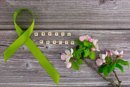 Lime green ribbon. Mental health awareness month concept mental health letters on old aged wooden background with blossom branches May green ribbon month to support mental health awarenessの写真素材