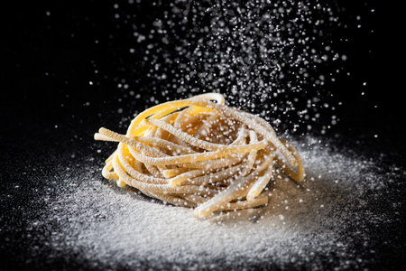 Uncooked traditional hand - rolled durum wheat pasta Pici of Tuscany, black background, macro photo of pasta pici and selective focus with white flour falling downの写真素材