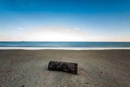 Wood remains on a  sand beach in front of the sea.  Long exposureの写真素材