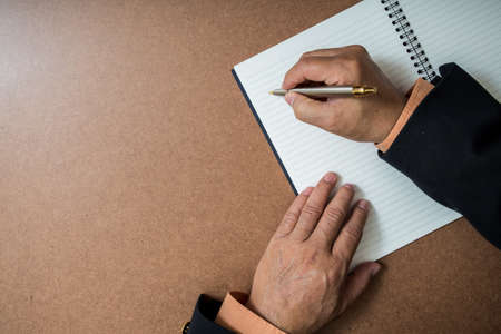 A business man  is writing in a big notepad on a wooden tableの写真素材