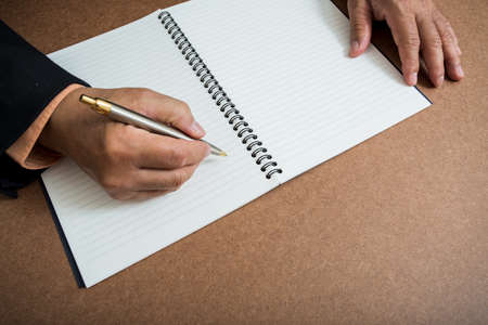A business man  is writing in a big notepad on a wooden tableの写真素材