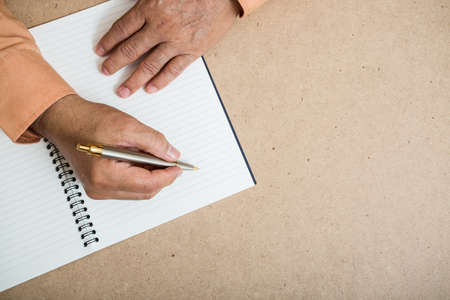 A business man  is writing in a big notepad on a wooden table