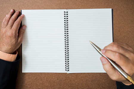 A business man  is writing in a big notepad on a wooden tableの写真素材