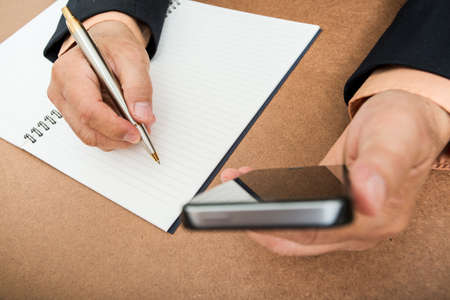 A business man  is writing in a big notepad on a wooden table