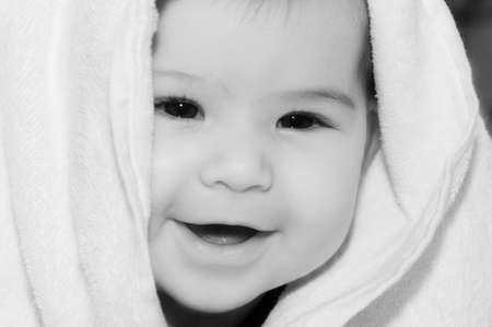 baby looking out and smiling from under blanketの写真素材