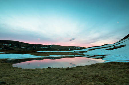 Landscape of lake with transparent water and distant mountains reflected in still morning watersの写真素材