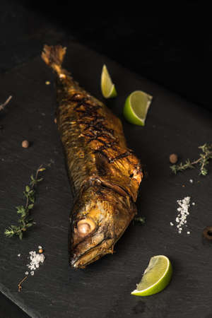 Delicious fresh fish on dark vintage background. Fish with aromatic herbs, spices and vegetables - healthy food, diet or cooking concept の写真素材