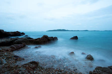 Dreamy wave crashing on rocky beach in twilight timeの写真素材