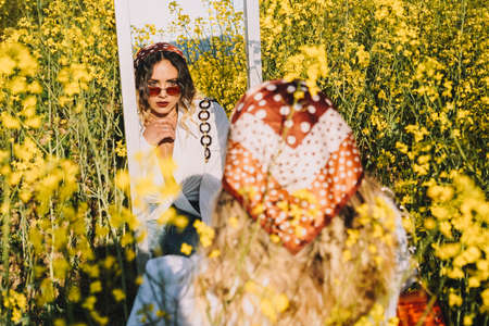 Beautiful woman with a headscarf looking at herself in a mirror on a sunny spring day by a field of flowersの写真素材