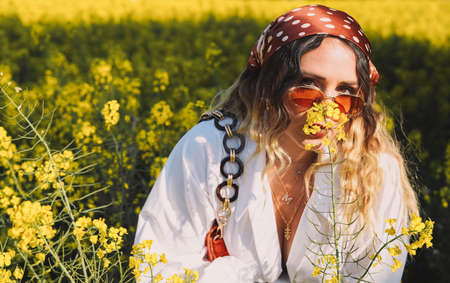 Beautiful woman with a headscarf walking on a sunny spring day through a field of flowersの写真素材