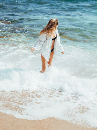 Young beautiful girl in a white swimsuit walks along the seashore