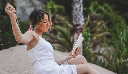 Beautiful and natural woman enjoying a book outdoors on the beach in summer. Vacation and adventure...