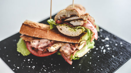 Sandwich with ham, cheese and vegetables on a black plate.