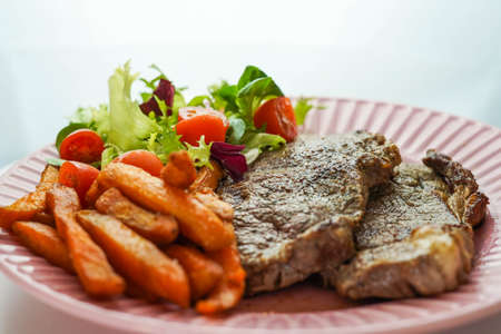 Combination plate of beefsteak with fried sweet potatoes and salad