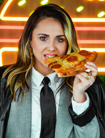 Young businesswoman eating pizza in a cafe with neon lights on backgroundの写真素材