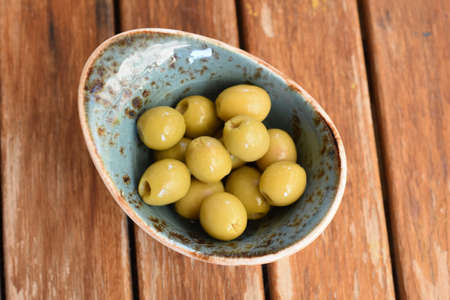 Olives in turquoise blue ceramic bowl on wooden tableの写真素材