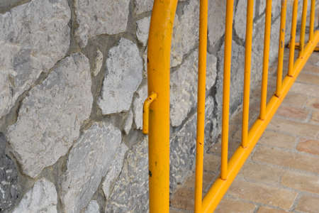 Yellow metal barrier on the street next to a stone wallの写真素材