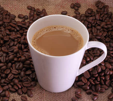 A cup of coffee milk and coffee beans on sack burlap background の写真素材