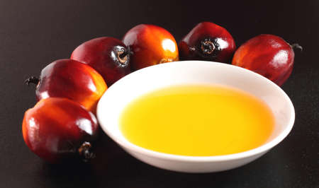 Oil palm fruits and a plate of cooking oil on black backgroundの写真素材