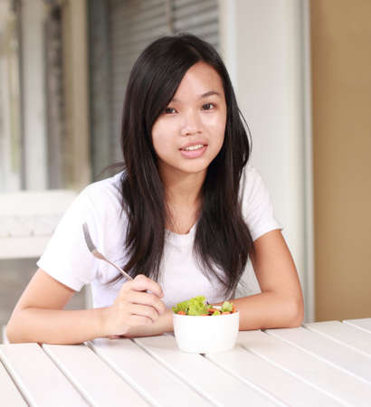 young lady eating vegetable salad at a restaurantの写真素材
