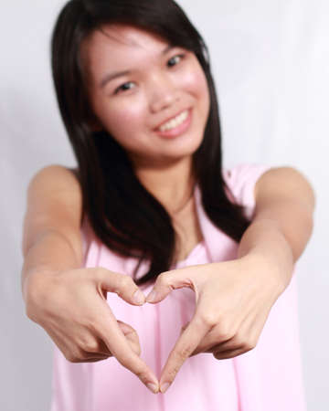 Beautiful and young lady forming a heart with her handsの写真素材