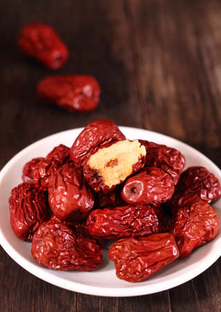 Dried chinese jujubes fruits with white plate on wooden tableの写真素材