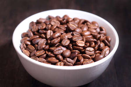 Coffee beans in white bowl isolated on brown wooden backgroundの写真素材