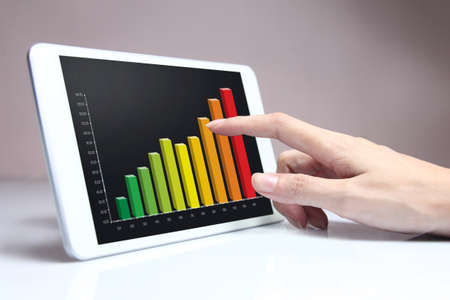 Hand pointing colorful business chart on tablet, representing business growth.の写真素材