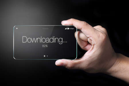 Transparent smartphone, downloading icon with hand on dark background.の写真素材