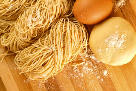 Handmade noodles and ingredients on chopping block. Noodles are an essential ingredient and staple in Chinese cuisine. の写真素材