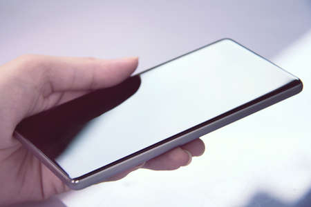 Hand holding mobile smartphone with blank screen. A smartphone is a mobile or cellular phone that runs off a mobile operating system and functions like a mini computer .の写真素材