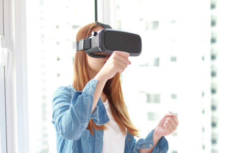 Young woman wearing virtual reality glasses at home. A virtual reality headset is a head-mounted...