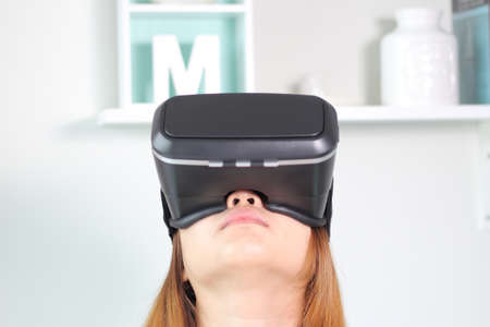 Young woman wearing virtual reality glasses at home. A virtual reality headset is a head-mounted...
