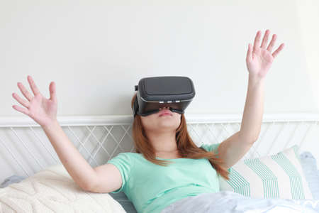 Young woman wearing virtual reality glasses at home. A virtual reality headset is a head-mounted...