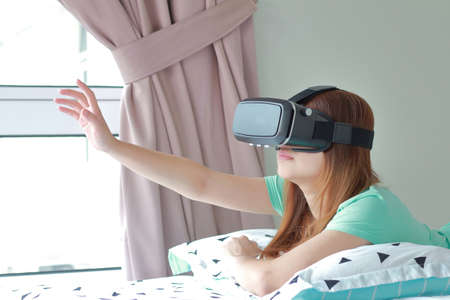 Young woman wearing virtual reality glasses at home. A virtual reality headset is a head-mounted...